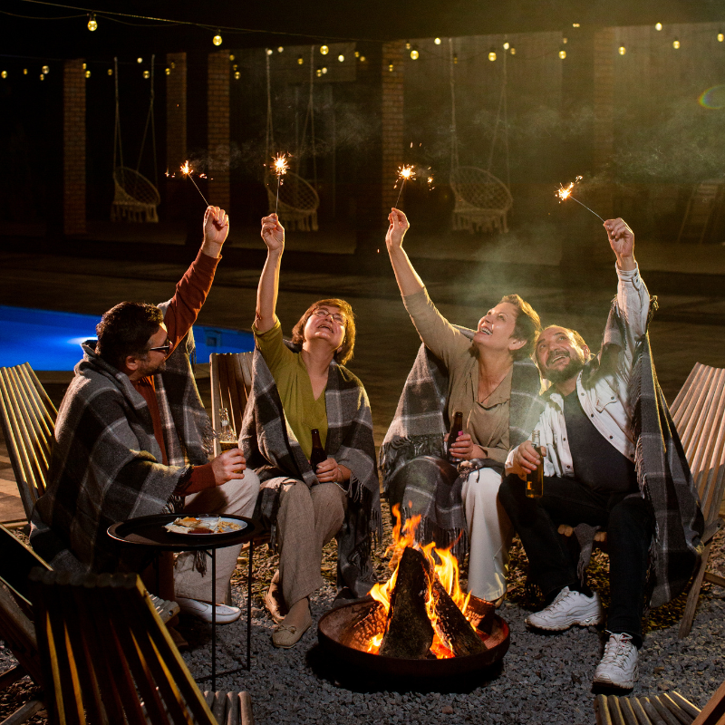 Friends holding sparklers by a poolside bonfire at night
